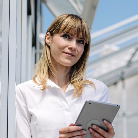 Thoughtful businesswoman holding digital tablet while standing by wall 