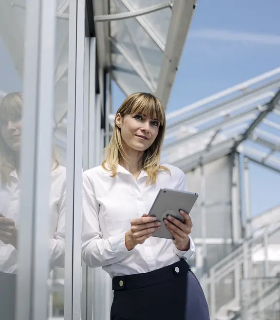 Thoughtful businesswoman holding digital tablet while standing by wall 