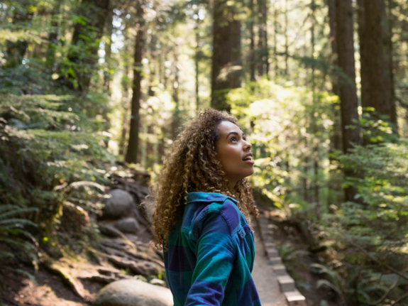 young woman hiking in the woods, looking up in awe