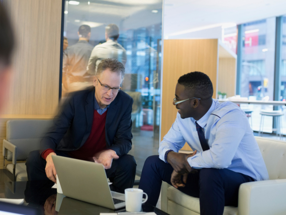two businessmen smiling and talking while looking at laptop